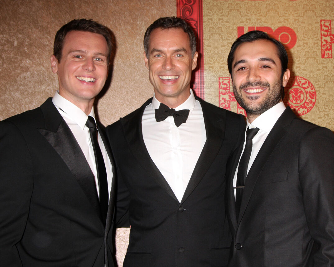 Jonathan Groff, Murray Bartlett, and Frankie J. Alvarez smile in black tuxedos on the red carpet.