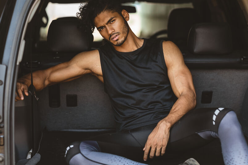 A muscular hunk posing for a thirst trap sitting on the trunk of his car. 