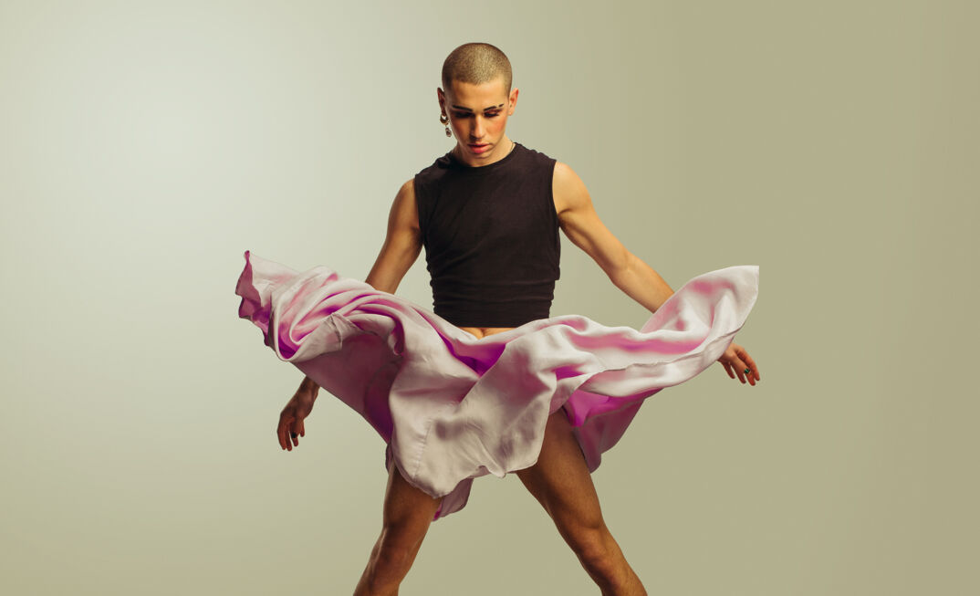 A young man jumping wearing black tank crop top and pink skirt. 