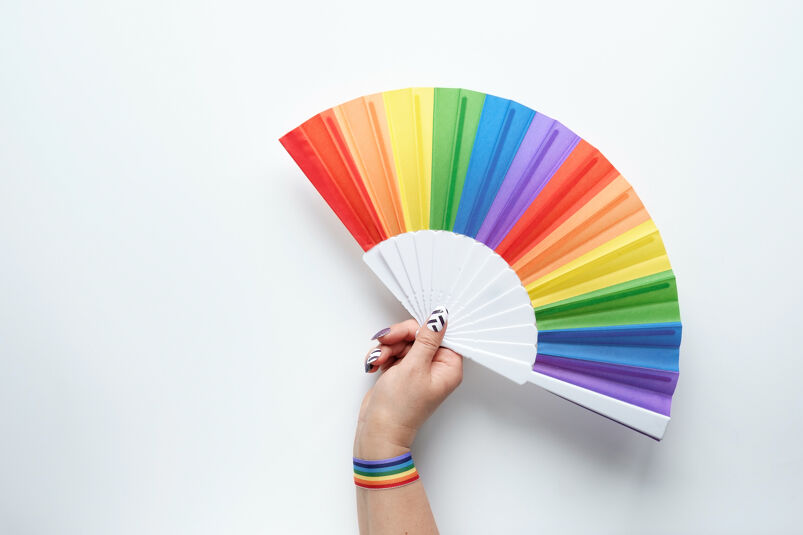 A hand holds a rainbow-colored folding fan, spread open.