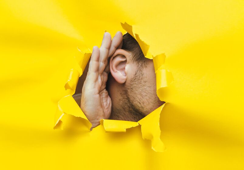 A man listening through a massive hole on a yellow wall. 