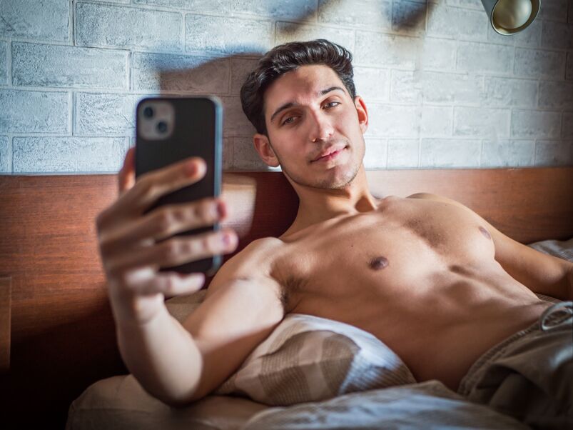 A shirtless man taking a selfie in bed. 