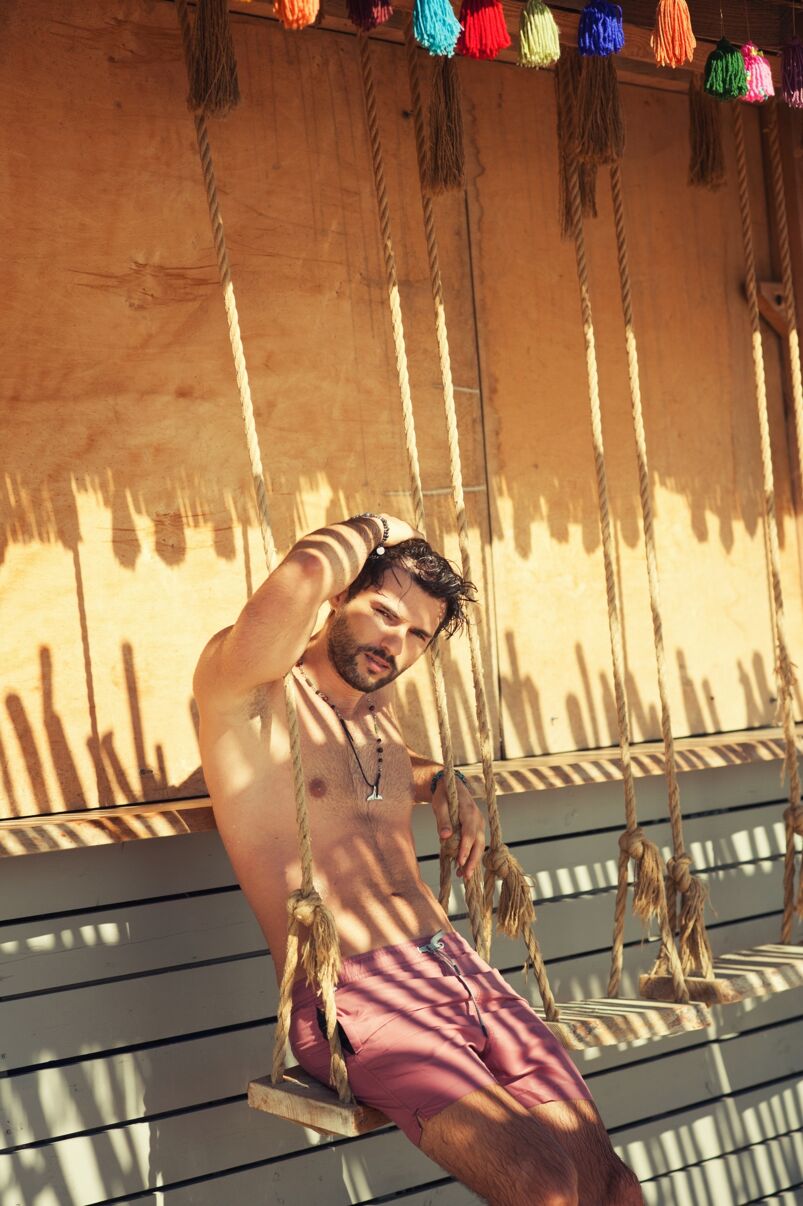 Man posing for photo on swing shirtless. 
