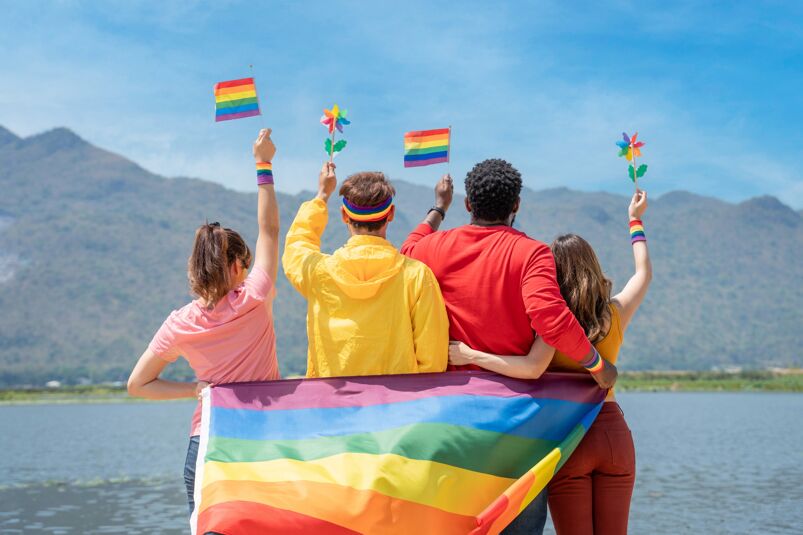 Four people waving rainbow symbols and holding each other. 
