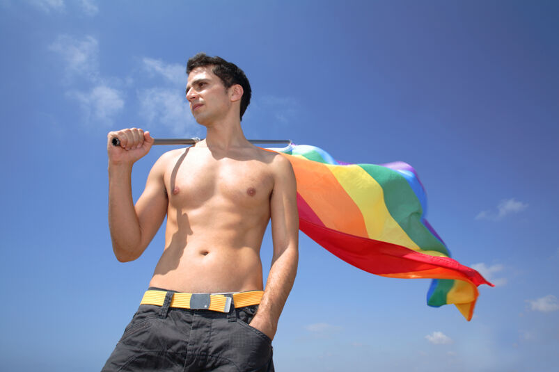 Shirtless guy holding Pride flag over his shoulder.
