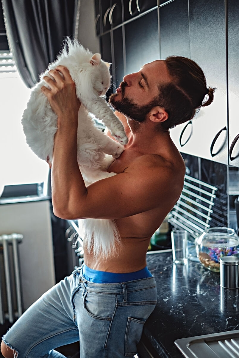 Cute guy with ponytail perking his lips at his cat. 