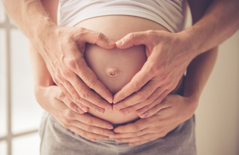 Masculine and feminine hands over a pregnant stomach. 