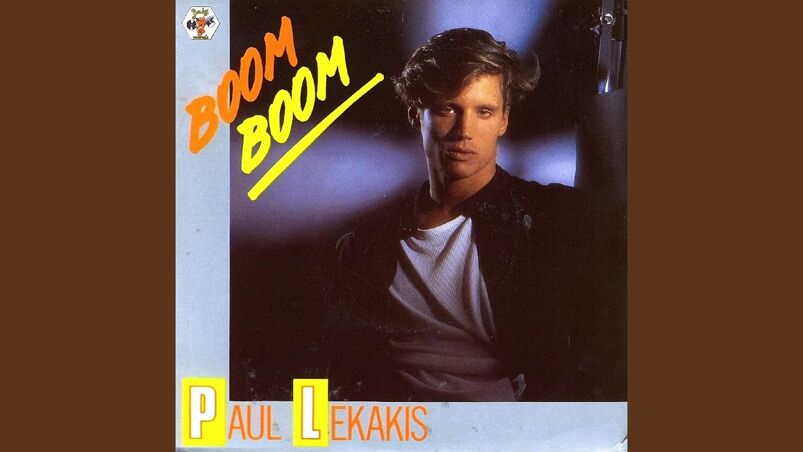 Paul Lekakis poses in dim lighting, wearing a leather jacket and white t-shirt in the cover for '80s single "Boom Boom."