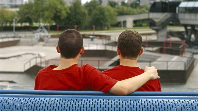 Two teen boys in red shirts sit on a bench that looks over their neighborhood.