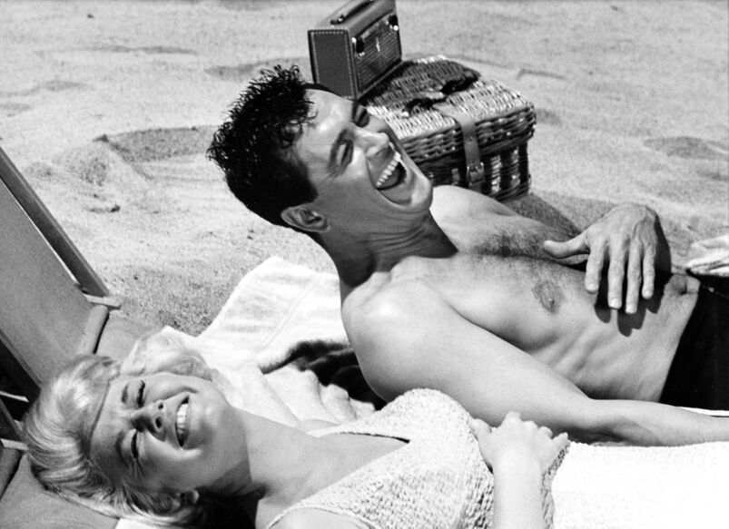 Doris Day and Rock Hudson sharing a laugh on the beach while filming 'Lover Come Back,' 1960.