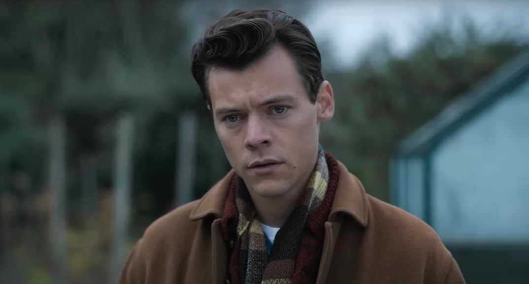 Harry Styles, wearing an overcoat and flannel, looks off blankly in a scene from 2022's 'My Policeman.'