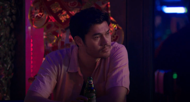 Henry Golding pensively looks on in purple lighting, holding a beer at the bar in 2020's 'Monsoon.'