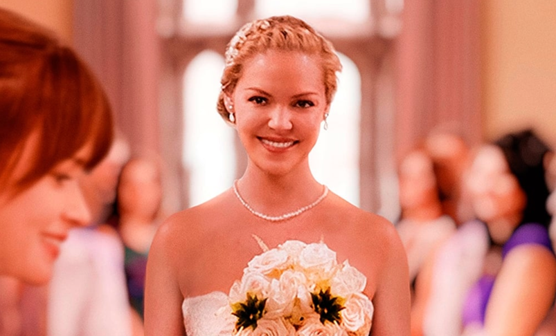 Katherine Heigl, wearing a white wedding gown and holding a bouquet, smiles as she walks down the aisle towards Alexis Bledel in the poster for 2015's 'Jenny's Wedding.'
