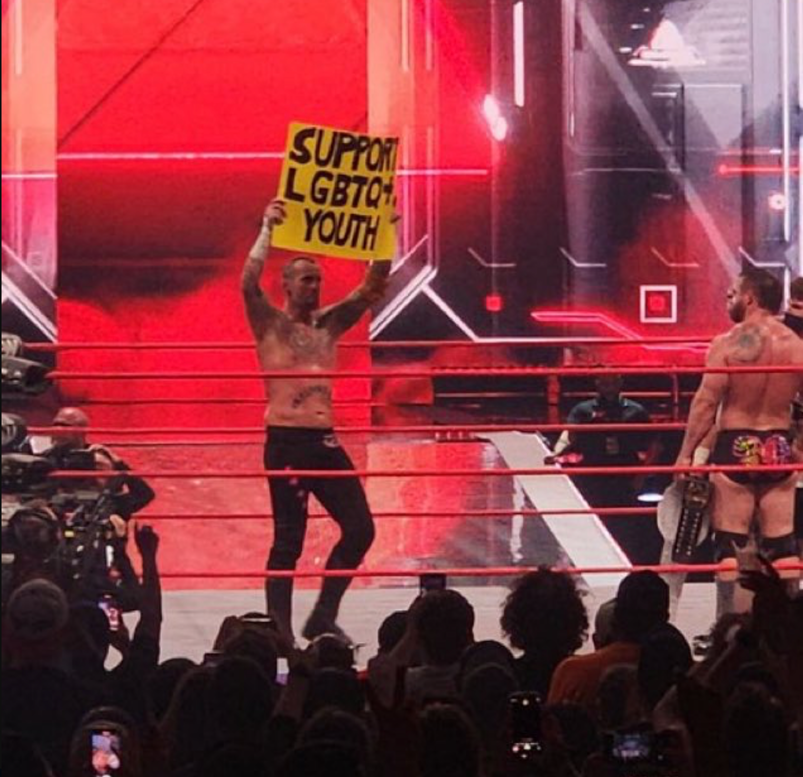 Wrestler CM Punk holding up a sign that says "support LGBTQ+ youth."