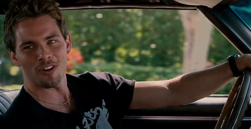 James Marsden, sporting highlighted spiky hair and a vintage tee, looks on while sitting in a car with his hand on the wheel in 'Sex Drive.'