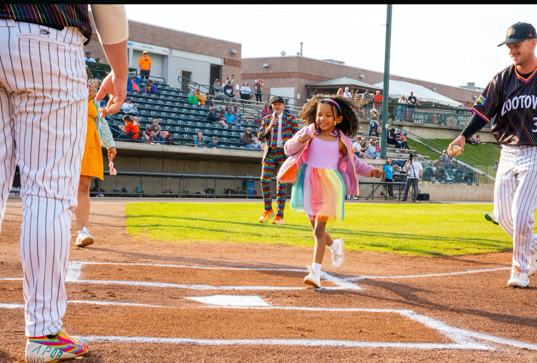 Young girl in a rainbow skirt running towards home plate.