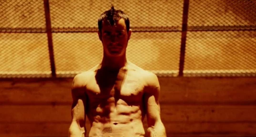Justin Theroux, with a dark mohawk, stands shirtless looking down at an industrial site in a scene from 'Charlie's Angels: Full Throttle.'