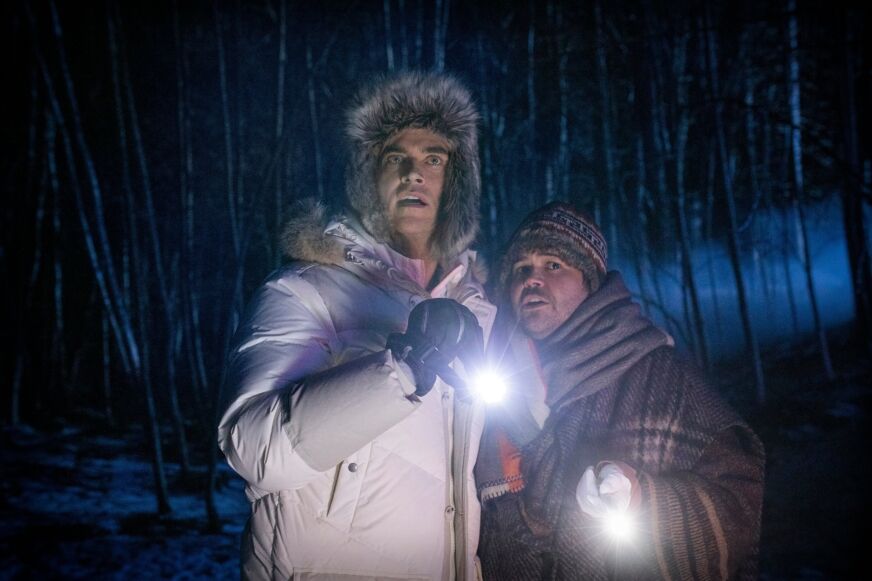 Cheyenne Jackson and Harvey Guillén wear coast in the snowy forest at night in 'Werewolves Within'