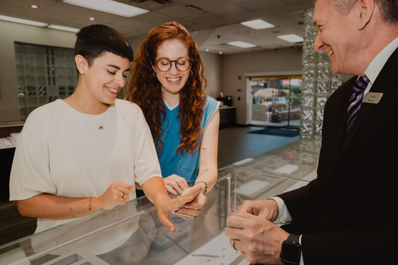 A female couple tries on wedding bands at a Shane Co. jewelry store.