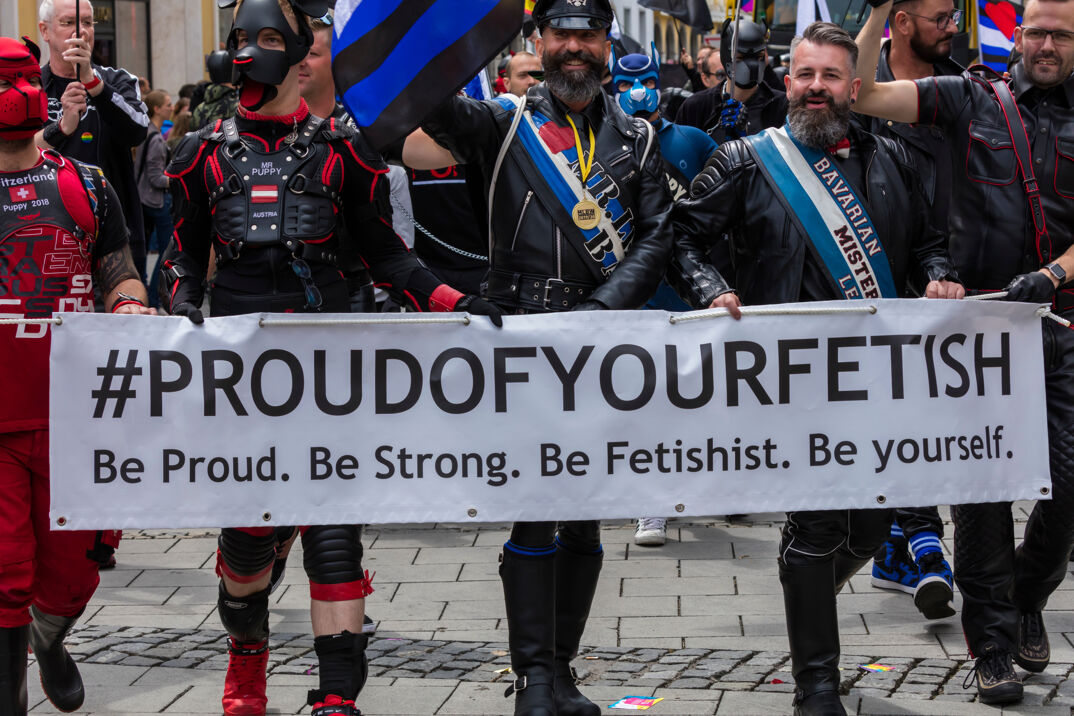 Leathermen at a fetish march holding a sign. 