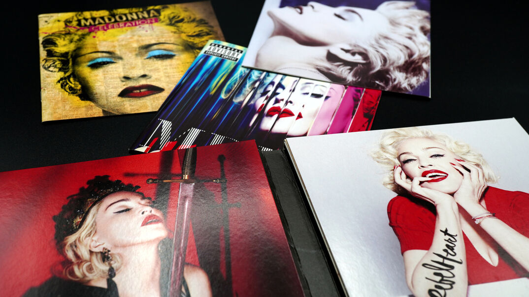 A collection of Madonna's vinyl records, including 'Dance,' 'MDNA,' 'Celebration,' and 'Rebel Heart,' sit in an assortment on a black table.