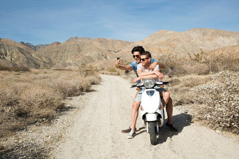 Two men on a moped in the desert taking a selfie. 