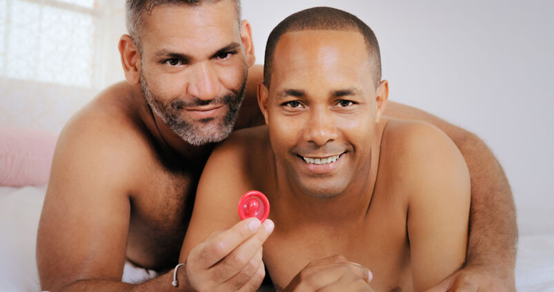 Homosexual couple smiling at camera holding a condom.
