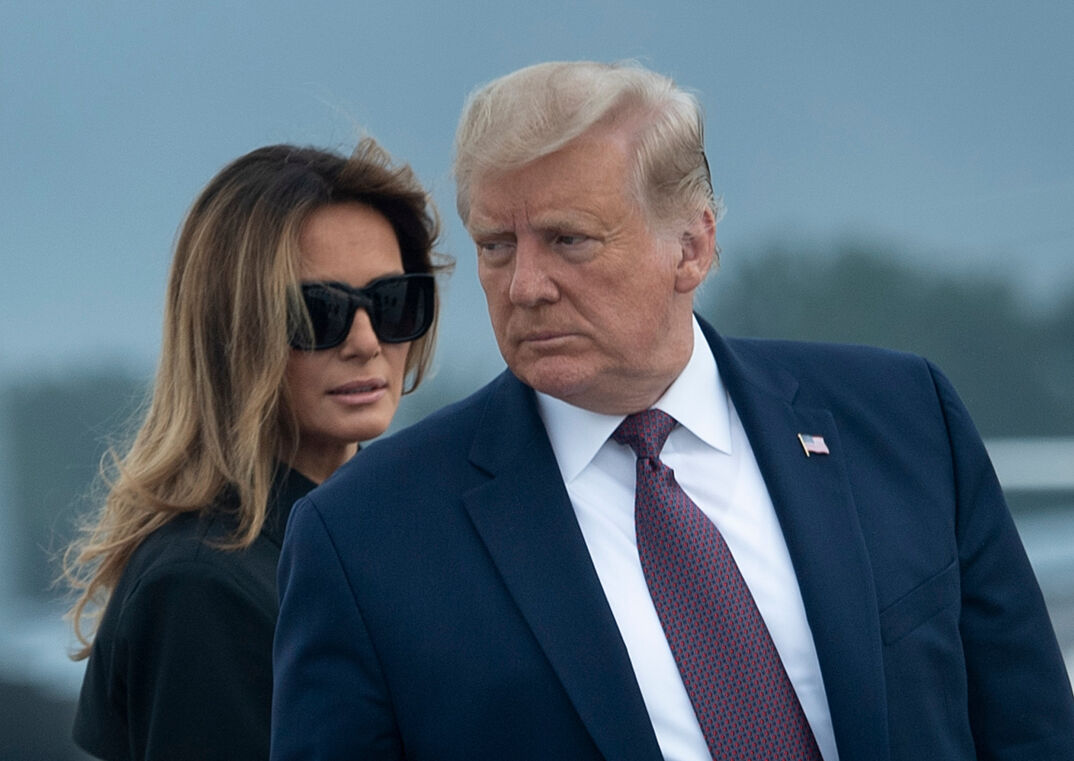 Donald Trump standing in front of Melania Trump, who's wearing black sunglasses. 