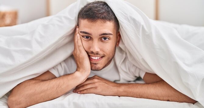A man lies under a comforter in bed