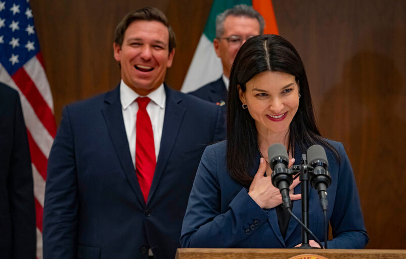 Florida's Republican Governor Ron DeSantis laughing in the background of a photo as he appoints Michelle Alvarez Barakat and Tanya Brinkley as judges to Miami’s Eleventh Judicial Circuit Court.