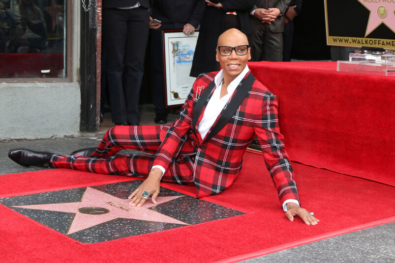 RuPaul wearing a red and black plaid suit laying on the Hollywood Walk of Fame.