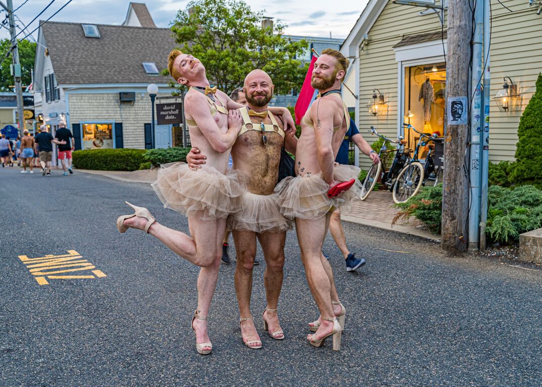 Three shirtless men in a khaki tutus on the street in Provincetown.