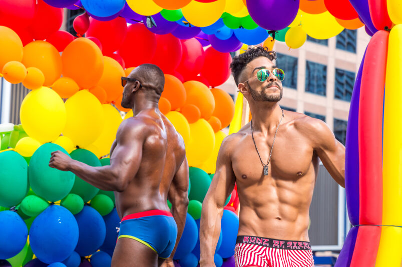 Two shirtless men dancing at a Pride festival. 