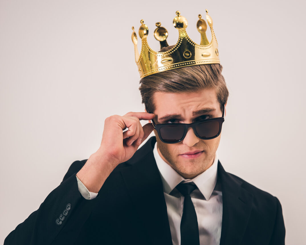 A man wearing a crown with sunglasses in a suit. 
