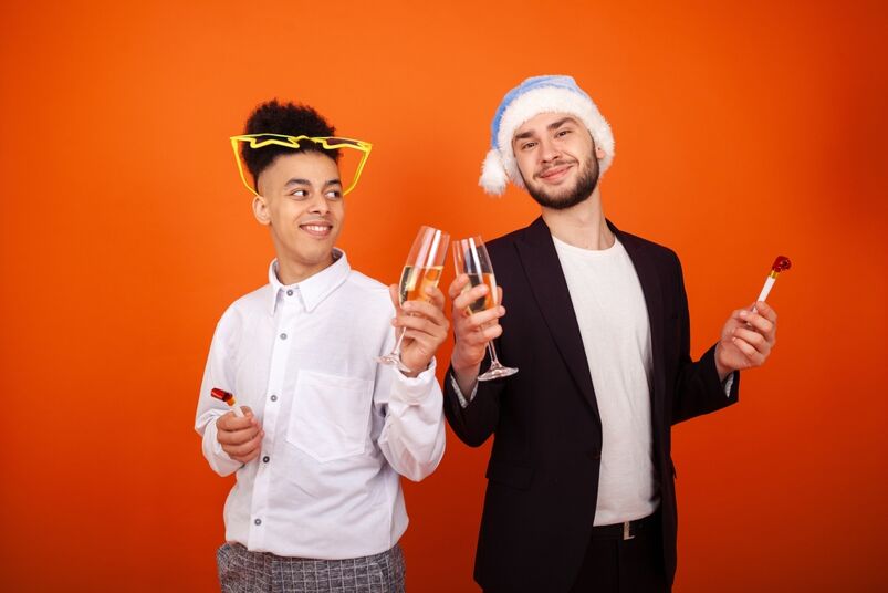 A queer couple celebrates New Years together. They are toasting drinks 
