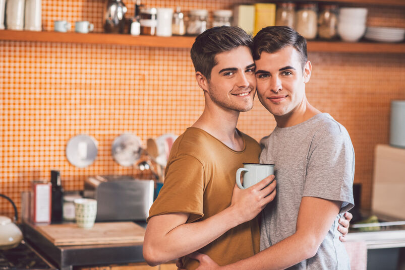 Gay couple embracing with a a coffee cup between them