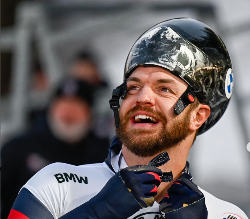 Andrew Blaser in his U.S. Skeleton uniform, wearing a black helmet and holding a black mouthguard. 