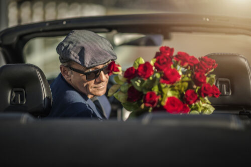 Sugar Daddy Eyes Seduction. Attractive Caucasian Men with Roses Awaiting His Girlfriend While Seating in a Convertible Car.