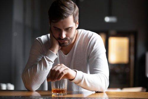 Upset young man drinker alcoholic sitting at bar counter with glass drinking whiskey alone
