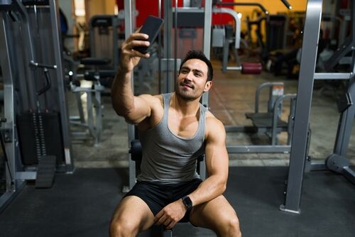 Straight equivalent to gay terms: Jock: Happy hispanic man taking a selfie with a smartphone to post on social media after working out at the gym