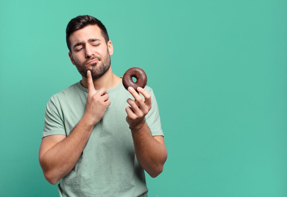 Straight men love anal stimulation: A young, handsome brunette man contemplates eating a chocolate donut.