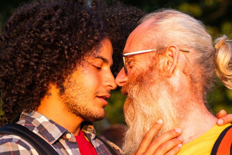 A gay couple of different ages and races share a joyful moment, embracing and smiling brightly amidst the serene beauty of nature
