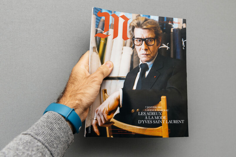 Gay fashion designers: Man holding M Magazine le monde with Yves Saint Laurent fashion icon on the cover