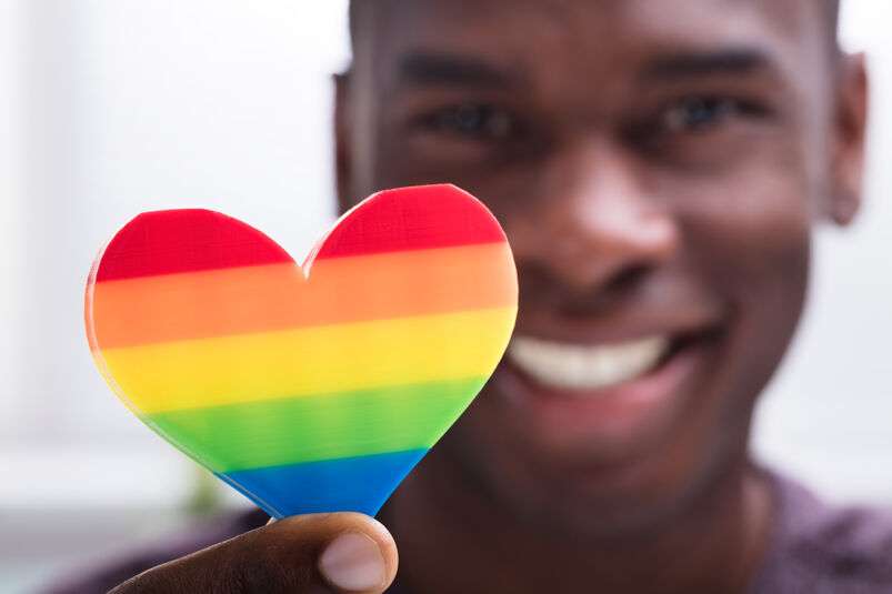 Being a good Daddy's boy: Smiling Man Holding Rainbow Heart In His Hand Against White Background