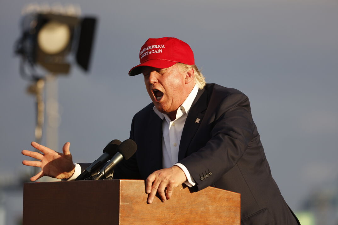Donald Trump wearing a red MAGA hat and yelling at a podium. 