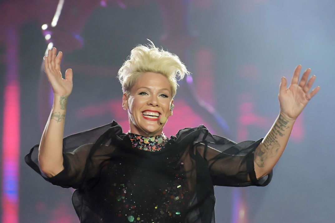 P!NK performing on stage wearing a black cover up over a shiny, multi-color dress. 