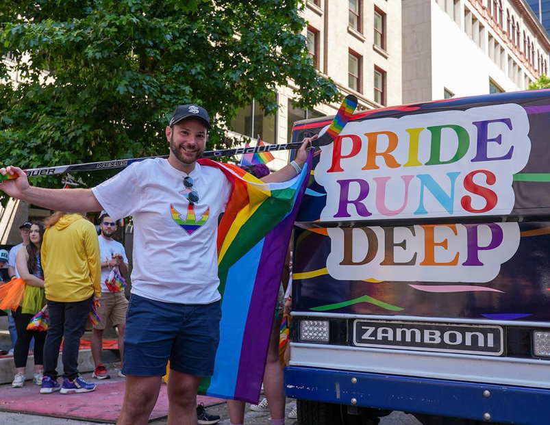 Seattle Kraken trainer Justin Rogers standing in front of a Zamboni during  Pride parade with the sign "Pride runs deep."