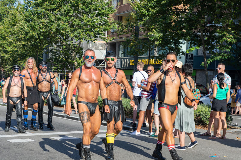 A group of daddies walking the street wearing leather harnesses. 