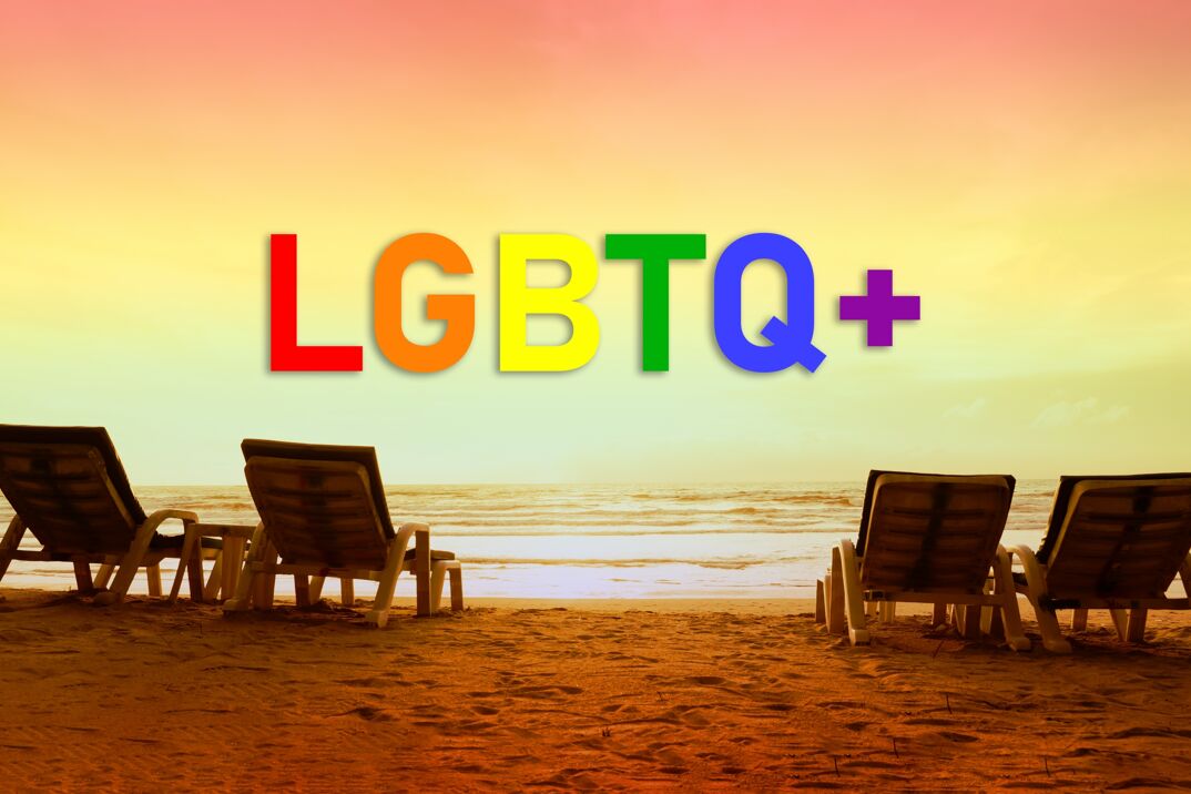The rainbow letters "LGBTQ+" on a beach with tanning beds during the sunset. 