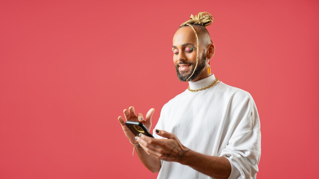 Black gay man with a beard wearing a stylish gray turtle neck typing on his iPhone.